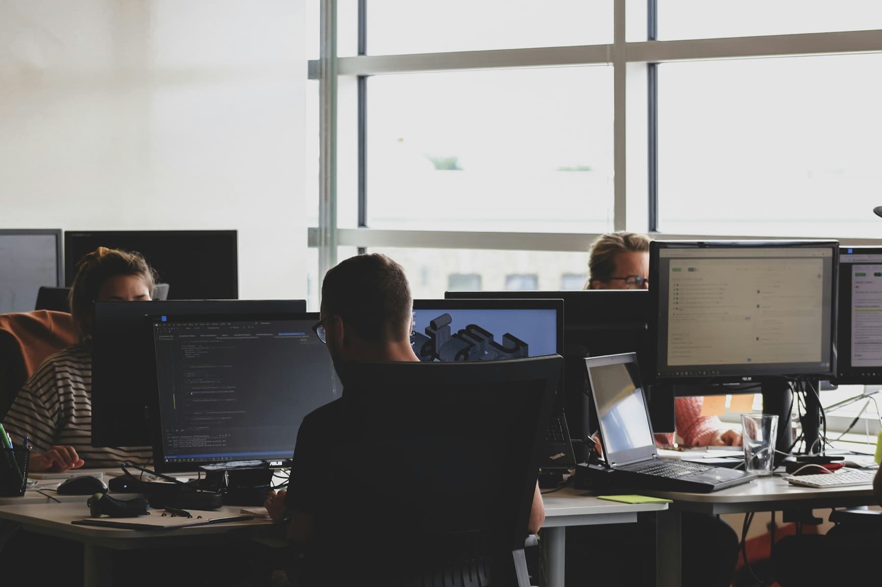 Developers at desks with code on their monitors